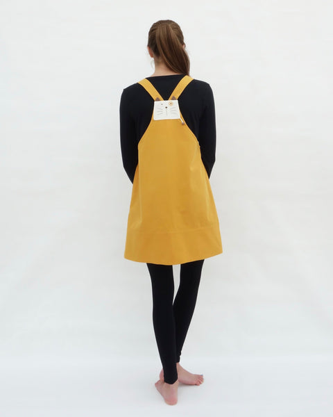 Woman wearing yellow, cat dress with cat appliqué, embroidery details, adjustable straps, in back view.