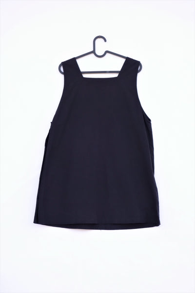 Cat Dress on a hanger, AKA pinafore dress, in black with cat appliqué, embroidery cat features, button enclosures down the left side in back view.