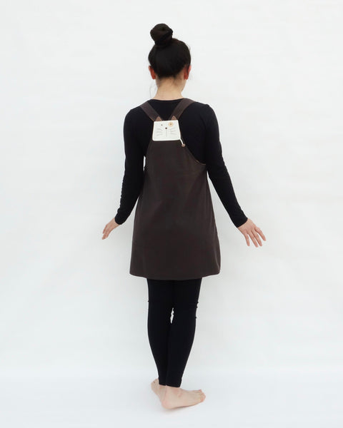 Woman wearing brown, cat dress with cat appliqué, embroidery details, adjustable straps, in back view.