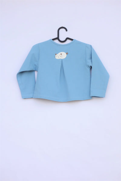 A blue girlsâ boxy-fit cotton cat jacket on a hanger with an appliquĂ© cat sleeping on the back. There is a pleat on the back of the jacket.
