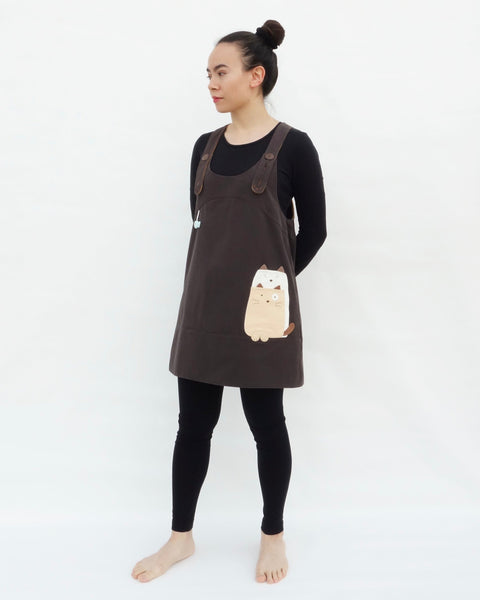 Woman wearing brown, cat dress with cat appliqué, embroidery details, adjustable straps, in 3/4 view.