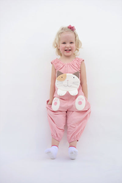 Girl with two hands in pockets and wearing a pink, cat-themed jumper with large, soft cat face pocket and cat paws in the front, two little fish friends swim on the back, sewn appliqué, embroidery details and side pockets in front view.