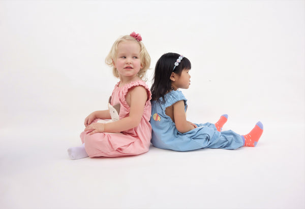 Two girls wearing pink and blue, cat-themed jumpers with large, soft cat face pockets and cat paws in the front, with two little fish friends swim on the back, sewn appliqué, embroidery details and side pockets in side view.