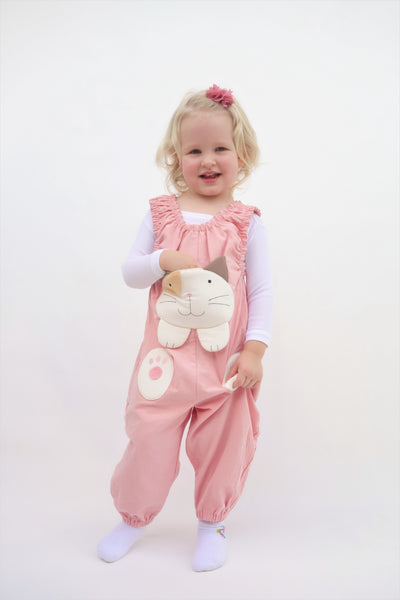 Girl with one hand tucked inside a pocket and a wearing pink, cat-themed jumper with large, soft cat face pocket and cat paws in the front, two little fish friends swim on the back, sewn appliqué, embroidery details and side pockets in front view.
