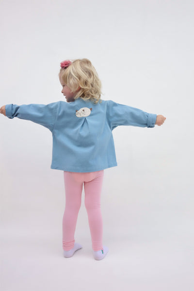 A girl is wearing a blue relaxed-fit cotton cat jacket with an appliqué sleeping cat on the back. Her arms are stretching out. There is a pleat on the back of the jacket.