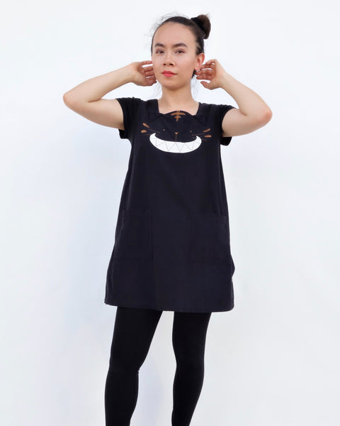 Women wearing a cat dress, AKA pinafore dress, in black with cat appliqué, embroidery cat features, button enclosures down the left side in front close-up view.