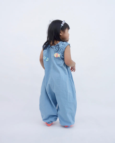 Girl wearing blue, cat-themed jumper with two sewn-on appliqué fish swimming on the back