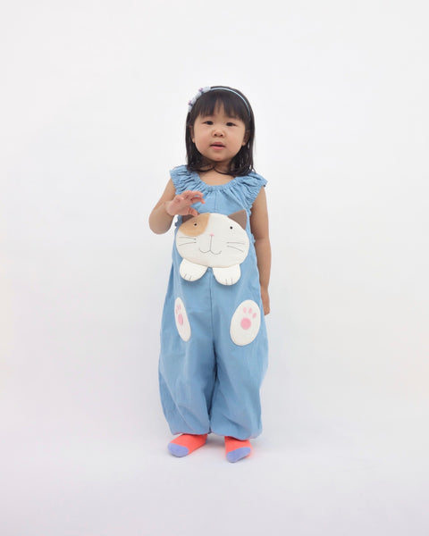 Girl wearing blue, cat-themed jumper with large, soft cat face pocket and cat paws in the front, two little fish friends swim on the back, sewn appliqué, embroidery details and side pockets in front view.