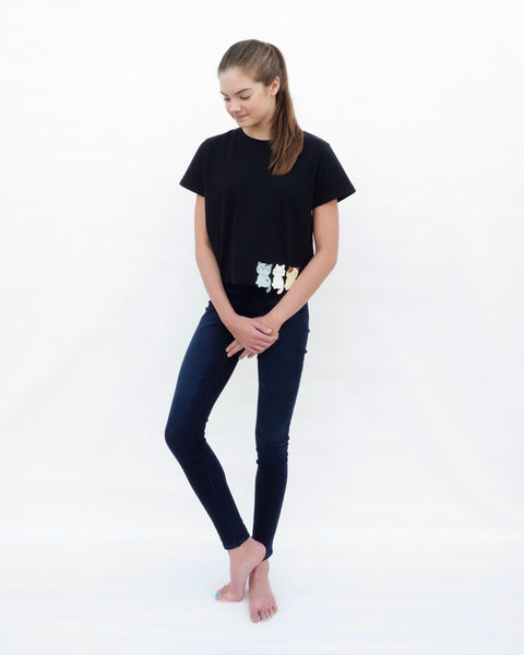 Woman looking down, wearing a Crop Top in black, with cat appliqué, embroidery details, short sleeves in full-body, close-up front view.