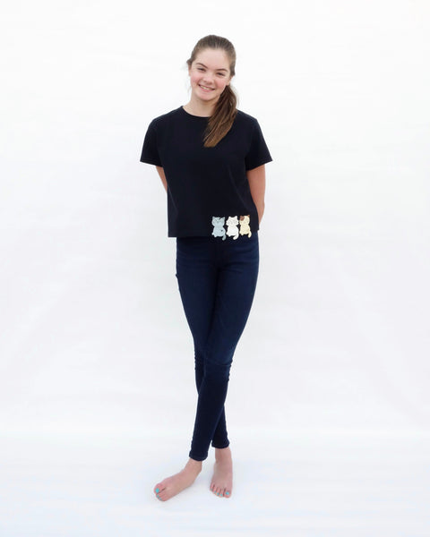 Woman wearing a Crop Top in black with cat appliqué, embroidery details, short sleeves in full-body, front view.
