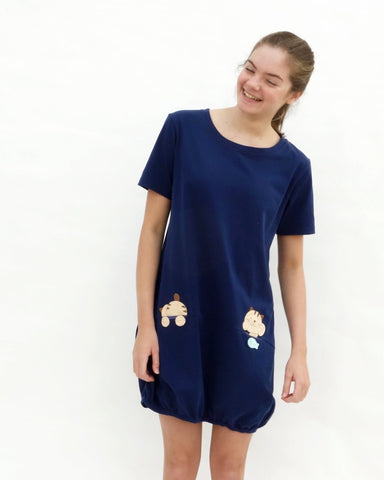 Woman wearing cat t-shirt dress in dark blue with cat appliqué, embroidery, front pockets, round neck opening, short sleeves, in front close-up view.