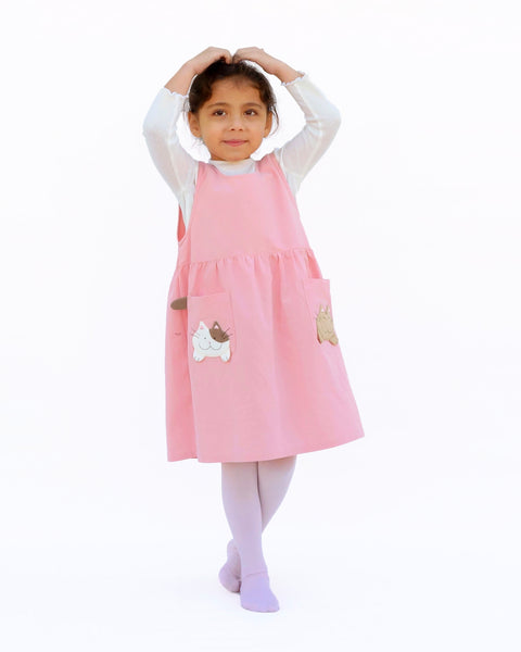 Cute girl wearing pink sleeveless cat dress with kittens and kitten tails on the pockets in front view.
