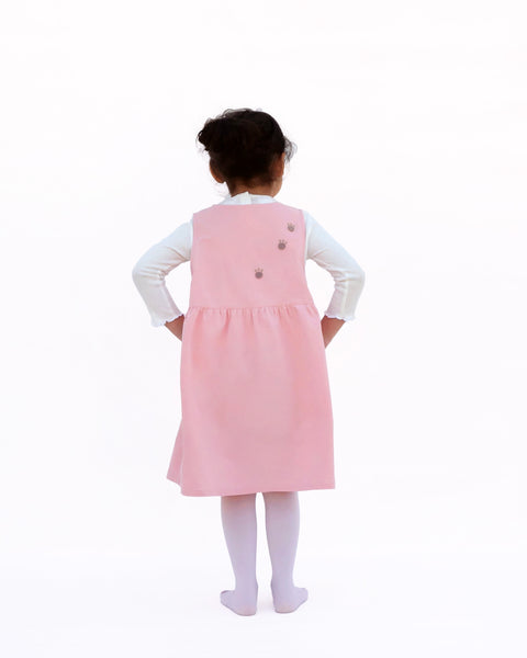 Girl wearing pink sleeveless cat dress with paw prints on back view.