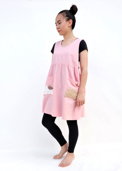 Woman wearing pink sleeveless cat dress with cats on pockets, standing and smiling