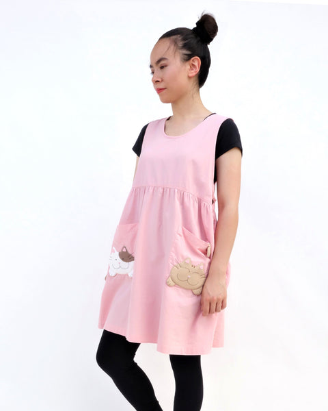 Woman wearing pink sleeveless cat dress with cats on pockets, standing and smiling