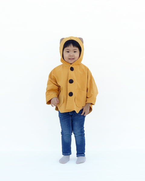 Toddler girl in golden yellow kitten cape coat jacket with cat ears and face on the hood, cat paw pockets, and buttons in the front