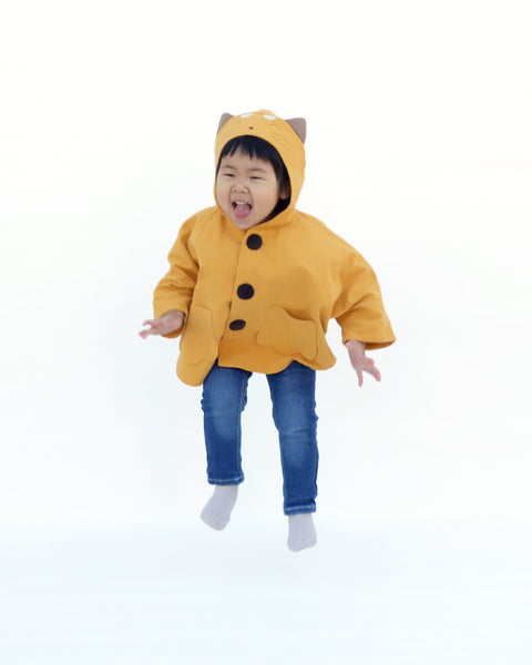 Toddler girl in golden yellow kitten cape coat jacket with cat ears and face on the hood, cat paw pockets, and buttons in the front
