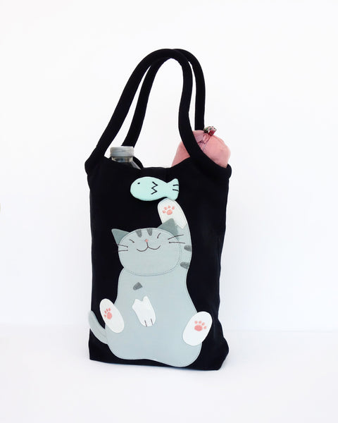 Cat Bottle-Tote in black with cotton interior, nylon lining, cat appliqué, embroidery detail, large main compartment, Velcro flap closure, sturdy double padded handles, squared off bottom for holding books, wallet, water bottle, pencil pouch, or umbrella.