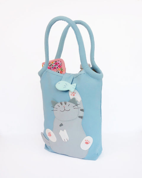 Cat Bottle-Tote in blue with cotton interior, nylon lining, cat appliqué, embroidery detail, large main compartment, Velcro flap closure, sturdy double padded handles, squared off bottom for holding books, wallet, water bottle, pencil pouch, or umbrella.
