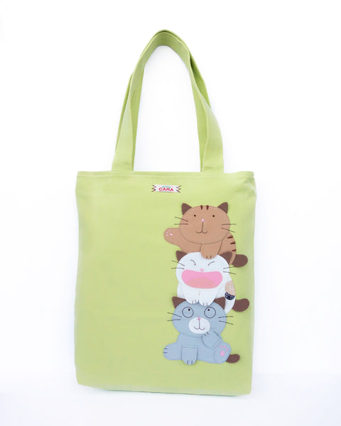 A light/spring green cat-themed canvas tote bag with three appliqué cats playfully stacked on top of each other