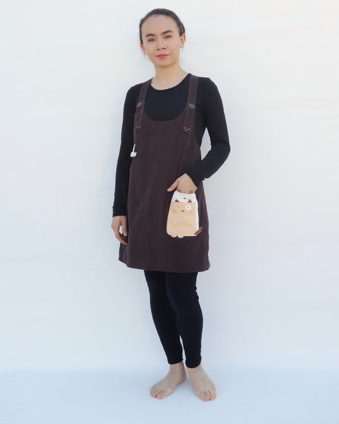 Woman wearing brown, cat dress with cat appliqué, embroidery details, adjustable straps, in front view.