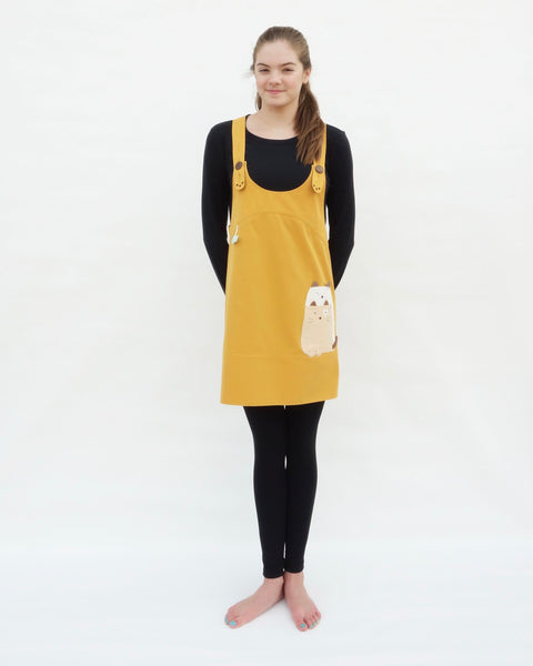 Woman wearing yellow, cat dress with cat appliqué, embroidery details, adjustable straps, in front view.