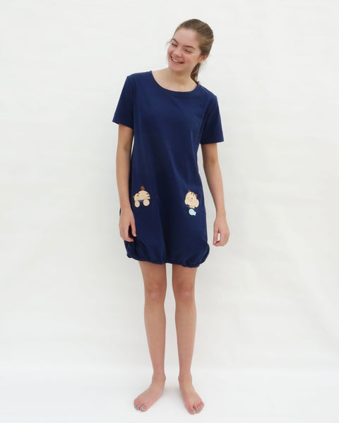 Woman wearing cat t-shirt dress in dark blue with cat appliqué, embroidery, front pockets, round neck opening, short sleeves, in front full-body view.