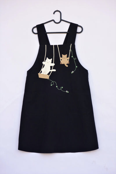 Cat Apron on a hanger with appliqué and embroidery details on front, two front pockets for storage in front view.