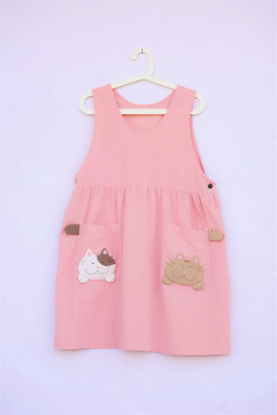 pink sleeveless cat dress with cats and cat tails on pockets, buttons on each side