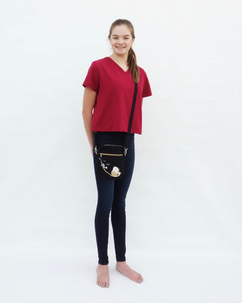 Woman wearing Cat Crop Top in red with V-neck, short sleeves, and crossbody purse in full-body, close-up front view.