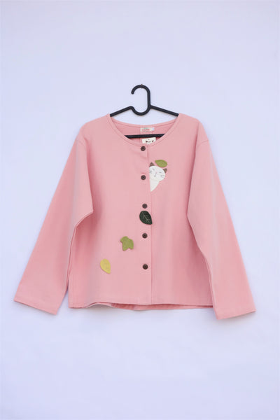 A pink women’s boxy-fit cotton cat jacket on a hanger with appliqué cat and leaves on the front. There are buttons on the jacket.