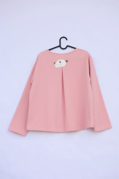 A pink womens’ boxy-fit cotton cat jacket on a hanger with an appliqué cat sleeping on the back. There is a pleat on the back of the jacket.