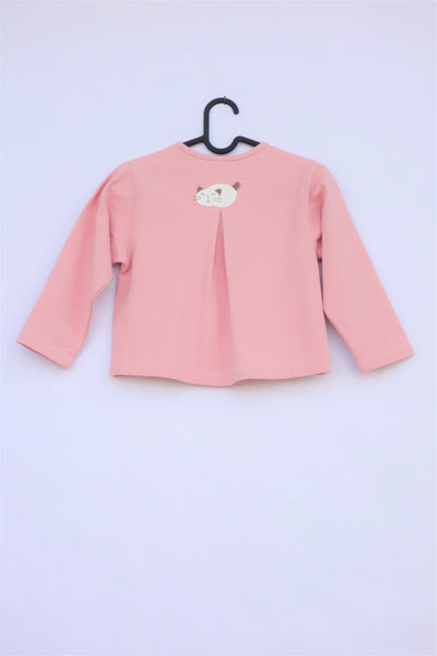 A pink girls’ boxy-fit cotton cat jacket on a hanger with an appliqué cat sleeping on the back. There is a pleat on the back of the jacket.