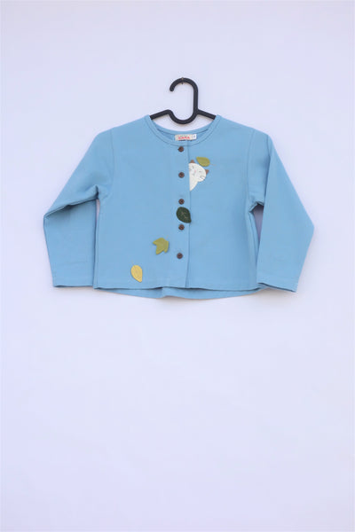 A blue girls’ boxy-fit cotton cat jacket on a hanger with appliqué cat and leaves on the front. There are buttons on the jacket.