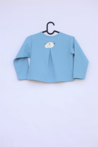 A blue girls’ boxy-fit cotton cat jacket on a hanger with an appliqué cat sleeping on the back. There is a pleat on the back of the jacket.