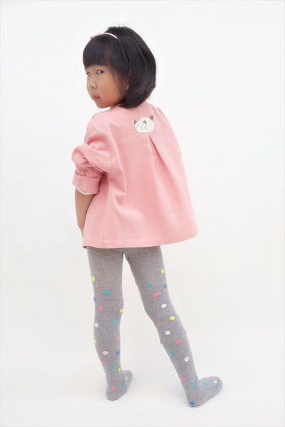 A girl looking over her shoulder and wearing a pink relaxed-fit cotton cat jacket with an appliqué peekaboo cat and falling leaves in the front. There is a pleat on the back of the jacket