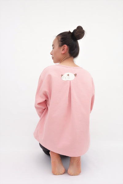 A woman is kneeling and wearing a pink cotton cat jacket with an appliqué cat sleeping on the back.