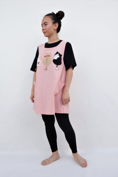A woman standing and wearing a cat-themed, cotton, pink shirt/mini A-line dress/top/tunic with three appliqué cats on the front