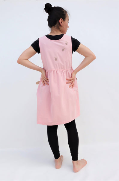 Woman wearing pink sleeveless cat dress with cat paw prints on the back of the dress, back facing and hands on hips