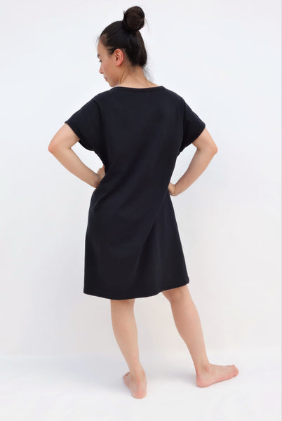 Woman wearing black, cat shift-dress with short sleeves, rounded neck opening in back view.