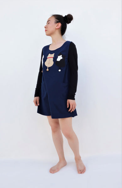 A woman standing and wearing a cat-themed, cotton, dark blue shirt/mini A-line dress/top/tunic with three appliqué cats on the front