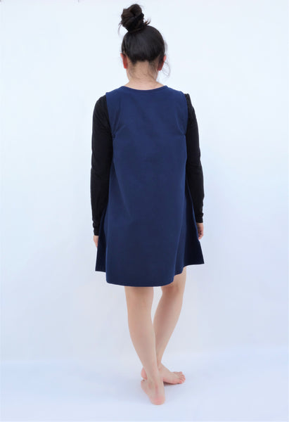 A woman standing and wearing a cat-themed, cotton, dark blue shirt/mini A-line dress/top/tunic, back view 