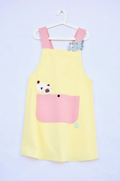 Pink and yellow color-blocked apron with cat appliqué, large front pocket, in front, flat view.