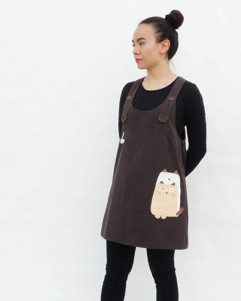 Woman wearing brown, cat dress with cat appliqué, embroidery details, adjustable straps, in 3/4 view.