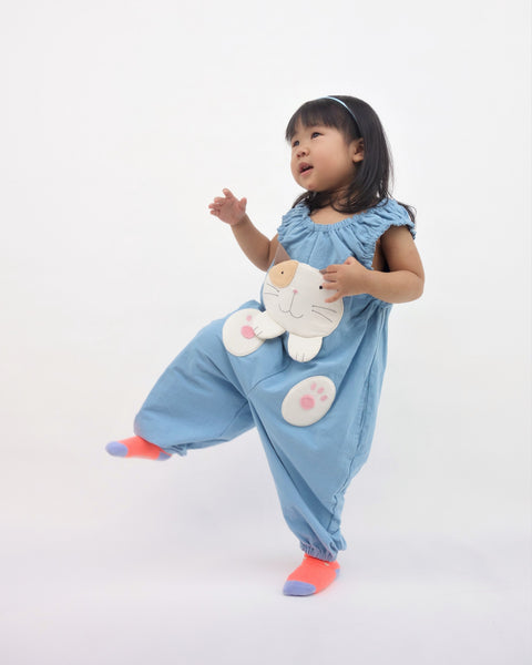 Girl pouncing in blue, cat-themed jumper with large, soft cat face pocket and cat paws in the front, two little fish friends swim on the back, sewn appliqué, embroidery details and side pockets in front view.