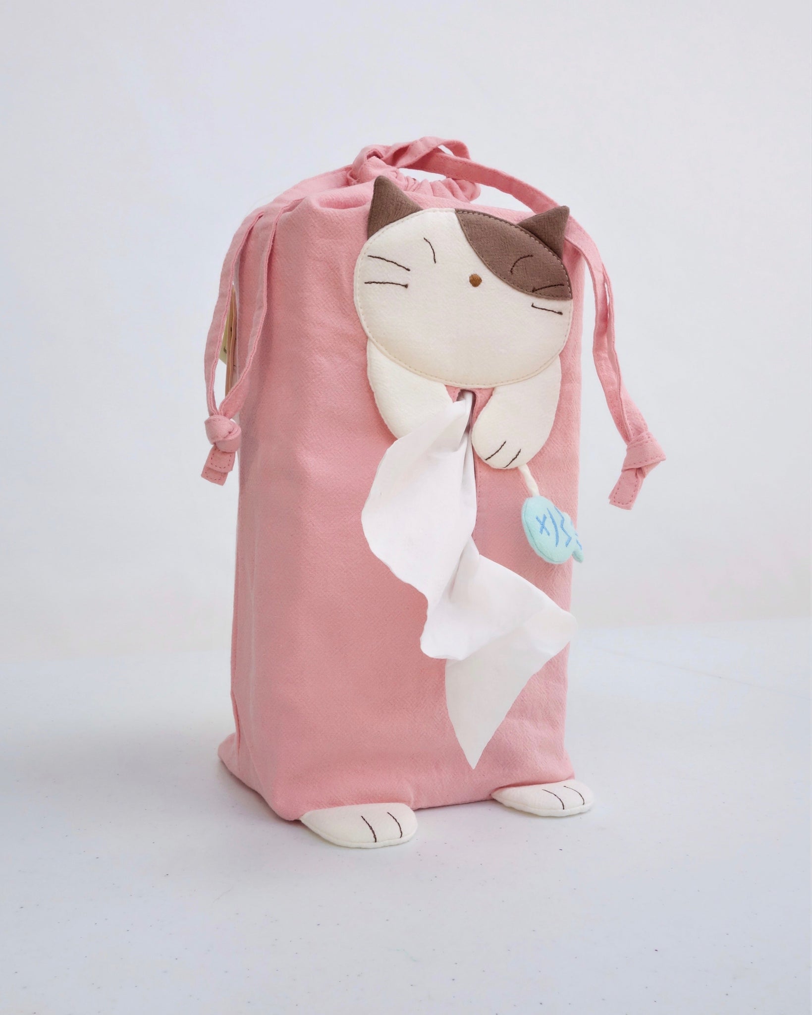 Cat tissue box cover in pink with drawstrings, two hanging straps, cat appliqué, fish charm, and cat feet, in front view.