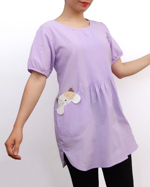 Woman wearing a lilac purple cotton cat-themed tunic dress for women with two cats/kittens on the pockets. The tunic dress has puffed sleeves and slits on the side. 