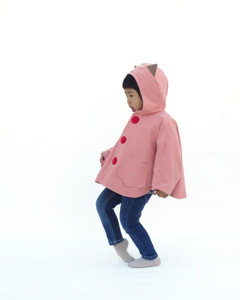 Toddler girl wearing pink kitten cape coat jacket with cat ears and face on the hood, cat paw pockets, and bright red buttons in side view.