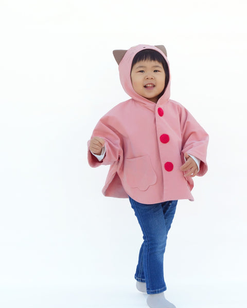 Toddler girl wearing pink kitten cape coat jacket with cat ears and face on the hood, cat paw pockets, and bright red buttons.