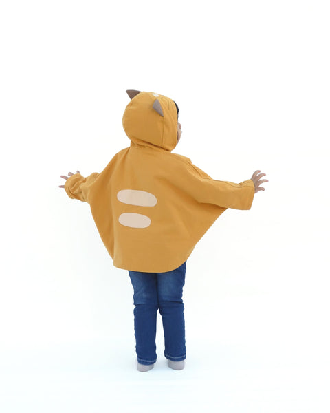 Toddler girl wearing golden yellow kitten cape coat jacket with cat ears and face on the hood, cat paw pockets, and two cat stripes in back view.